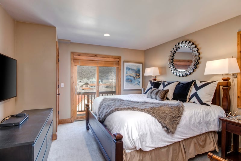 Elegant master bedroom with plush bedding, TV, and balcony views outside.