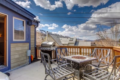 Outdoor patio with grill, fire pit table, and mountain backdrop.