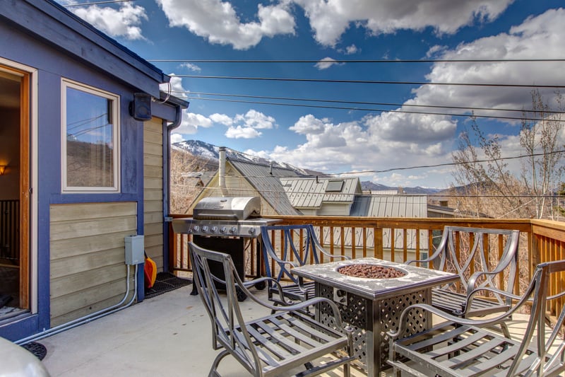 Outdoor patio with grill, fire pit table, and mountain backdrop.