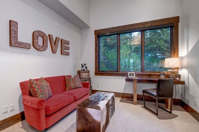 The den offers a cozy spot to read, work, or unwind with forest views, a writing desk, and inviting lounge seating.