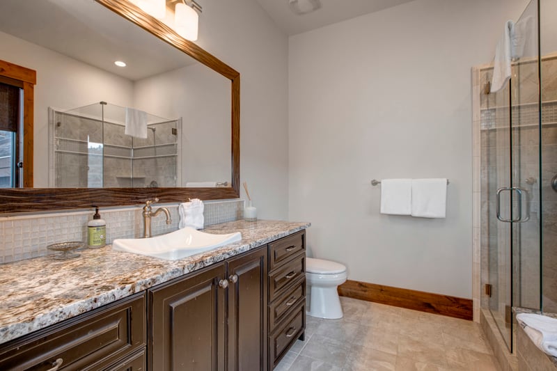 Modern bathroom with granite counters, glass shower, and warm wood trim.