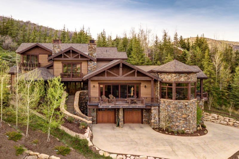 Elegant rustic home with balcony, stone turret, and forest backdrop.