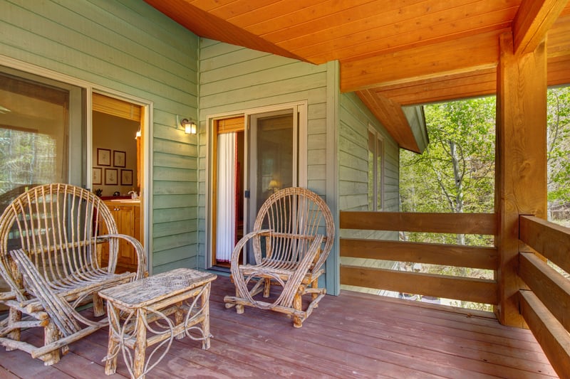 Covered balcony offers shaded seating and wooded views for year-round enjoyment, access through family room.