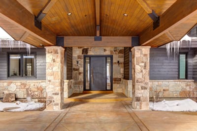Covered stone entry with warm wood beams creates a welcoming mountain lodge vibe.