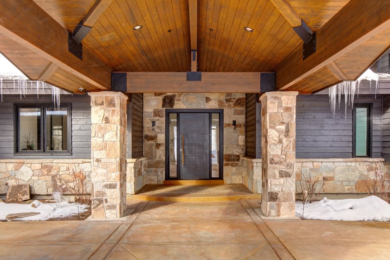Covered stone entry with warm wood beams creates a welcoming mountain lodge vibe.