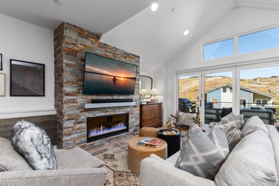 Gather around the gas fireplace in the stylish living room with large windows and sectional seating for movie nights or cozy chats. PEA-1009