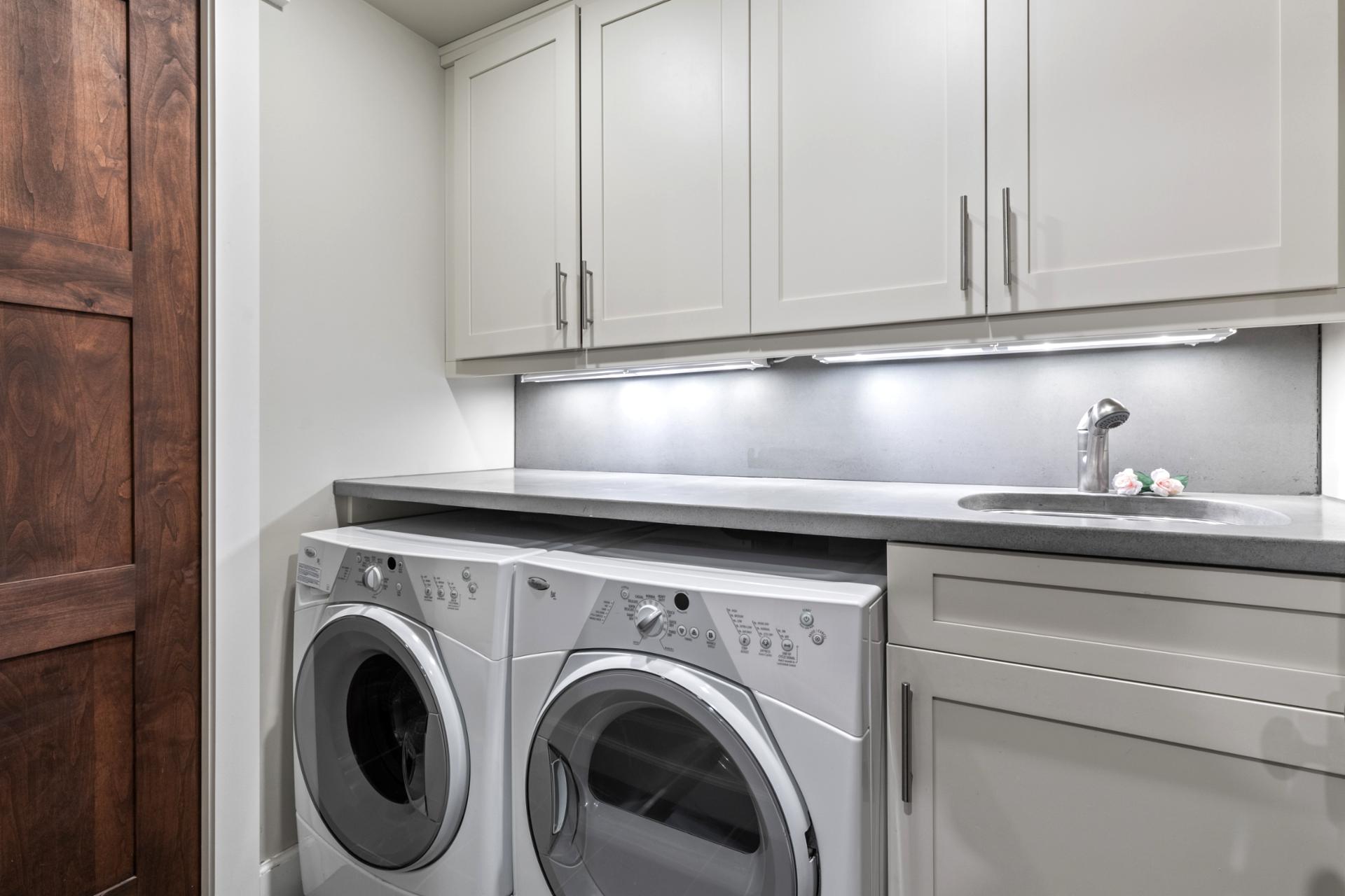 Main laundry room with full-size machines, sink, and sleek cabinetry.