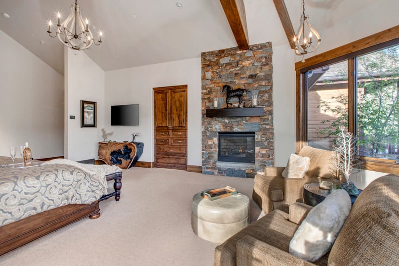 Exposed beams, gas fireplace, reading area, and rich wood details make this primary suite feel like a luxury mountain lodge.