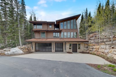 Modern alpine exterior with attached garage and forest setting.