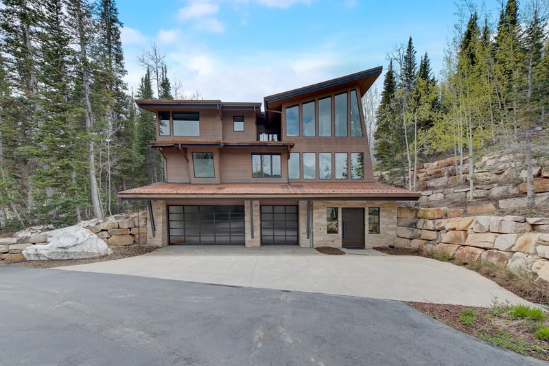 Modern alpine exterior with attached garage and forest setting.