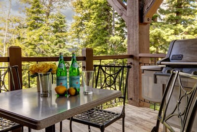 Enjoy drinks and grilled meals on the shaded balcony with forest backdrop.