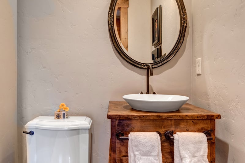 Half bath with circular mirror and pedestal sink for guests’ convenience.