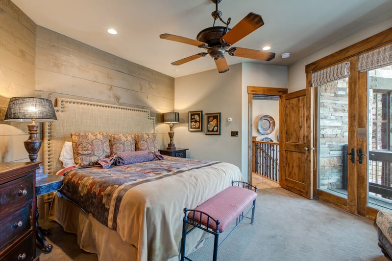 A second view of this main-level suite reveals soft beige bedding, a ceiling fan, and private patio access.