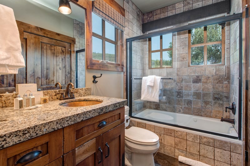 This ensuite bath includes a granite vanity, tiled shower/tub combo, and warm wood finishes throughout.