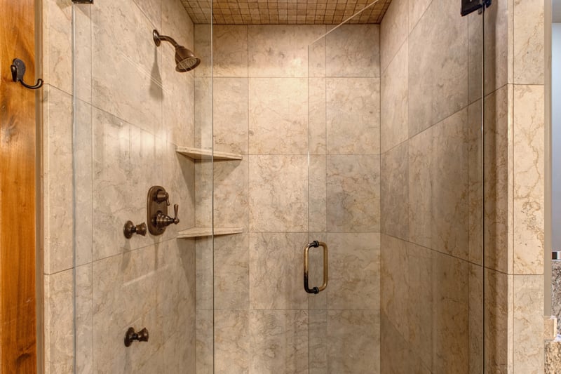 The primary bath includes a spacious tiled shower with bronze fixtures, a glass door, and warm wood trim.