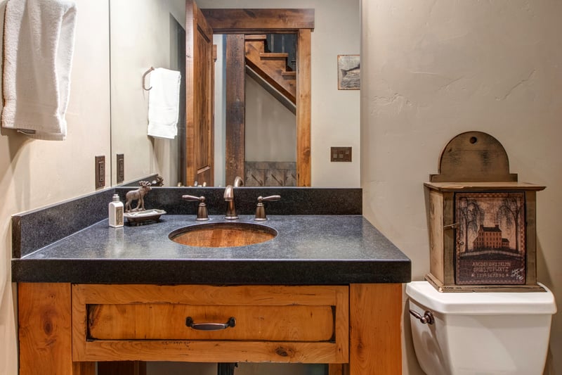 This main-level powder room features a rustic wood vanity, stone counter, and warm mountain character.