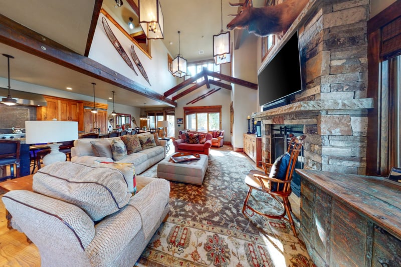 This expansive living area connects to the dining and kitchen spaces, with lodge-style beams and a warm, rustic aesthetic.