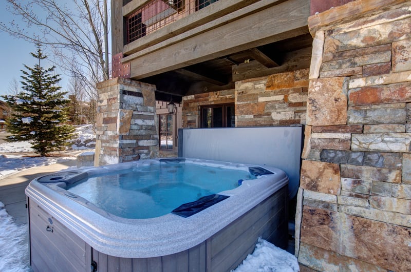 Unwind in your private outdoor hot tub tucked beside rustic stone columns and pine trees. Perfect after mountain adventures.