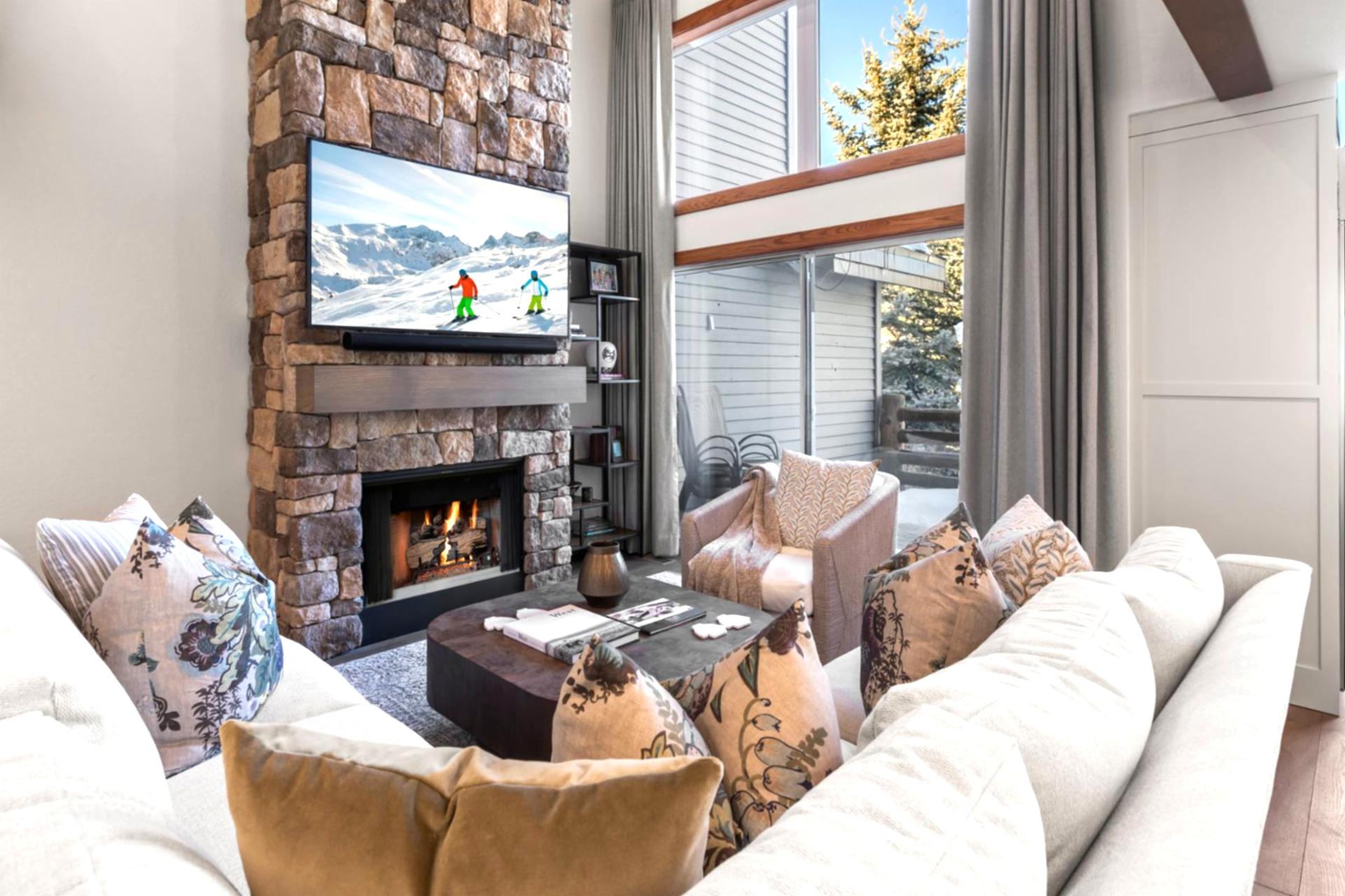 Cozy winter retreat with plush seating, stone fireplace, and mountain views through soaring windows.