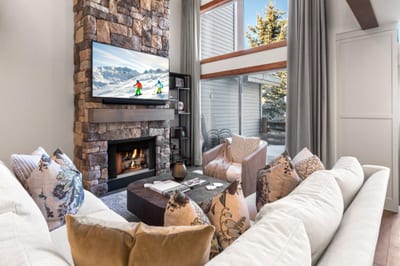 Cozy winter retreat with plush seating, stone fireplace, and mountain views through soaring windows.