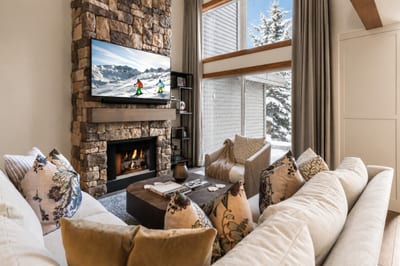 Cozy winter retreat with plush seating, stone fireplace, and mountain views through soaring windows.