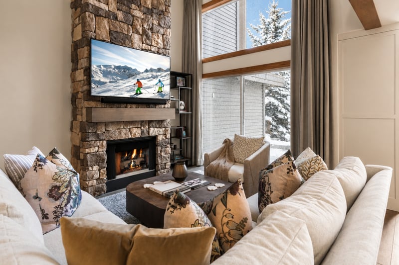 Cozy winter retreat with plush seating, stone fireplace, and mountain views through soaring windows.