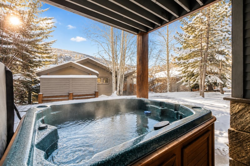 Cozy outdoor hot tub retreat with snowy mountain views and evergreen trees.