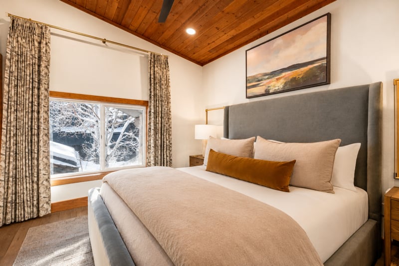 Tranquil king suite with cozy bedding, vaulted wood ceiling, and scenic snow-covered view.