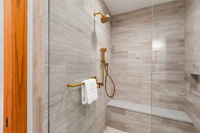 Spa-inspired shower with sleek tile, built-in bench, and gold fixtures for a luxurious touch.