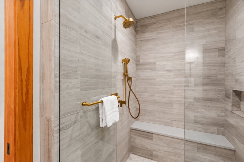 Spa-inspired shower with sleek tile, built-in bench, and gold fixtures for a luxurious touch.