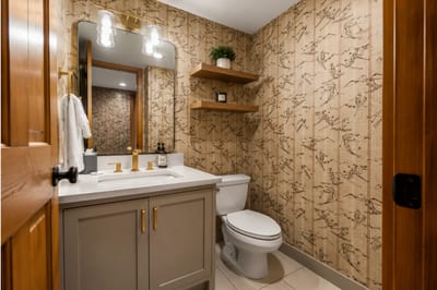 Stylish powder room with ski-themed wallpaper, gold fixtures, and a clean modern touch.