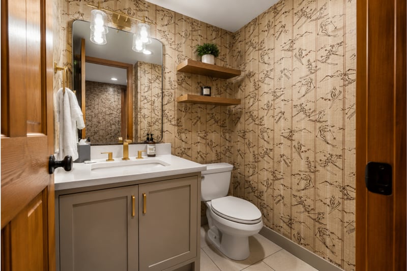 Stylish powder room with ski-themed wallpaper, gold fixtures, and a clean modern touch.
