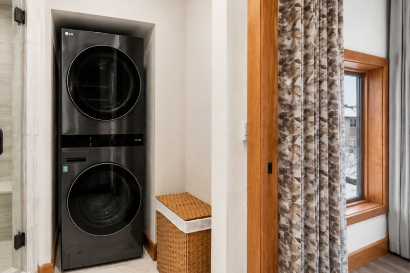 Sleek laundry space with stacked LG washer-dryer, wicker basket, and robe storage.