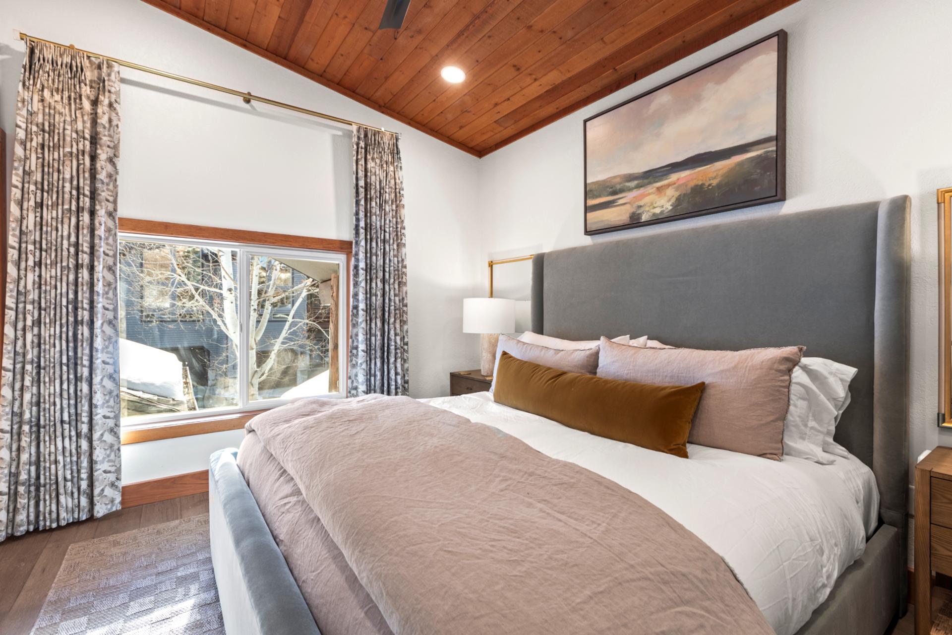 Tranquil king suite with cozy bedding, vaulted wood ceiling, and scenic snow-covered view.