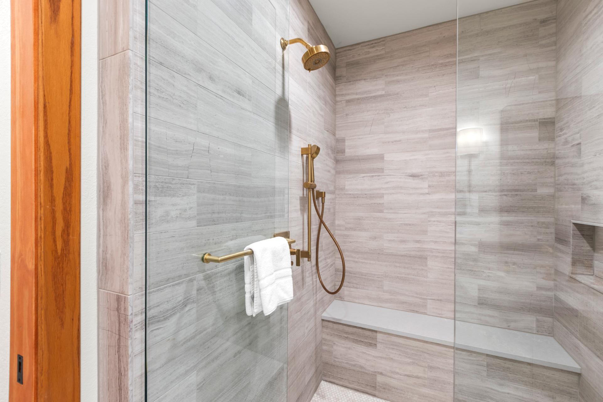 Spa-inspired shower with sleek tile, built-in bench, and gold fixtures for a luxurious touch.