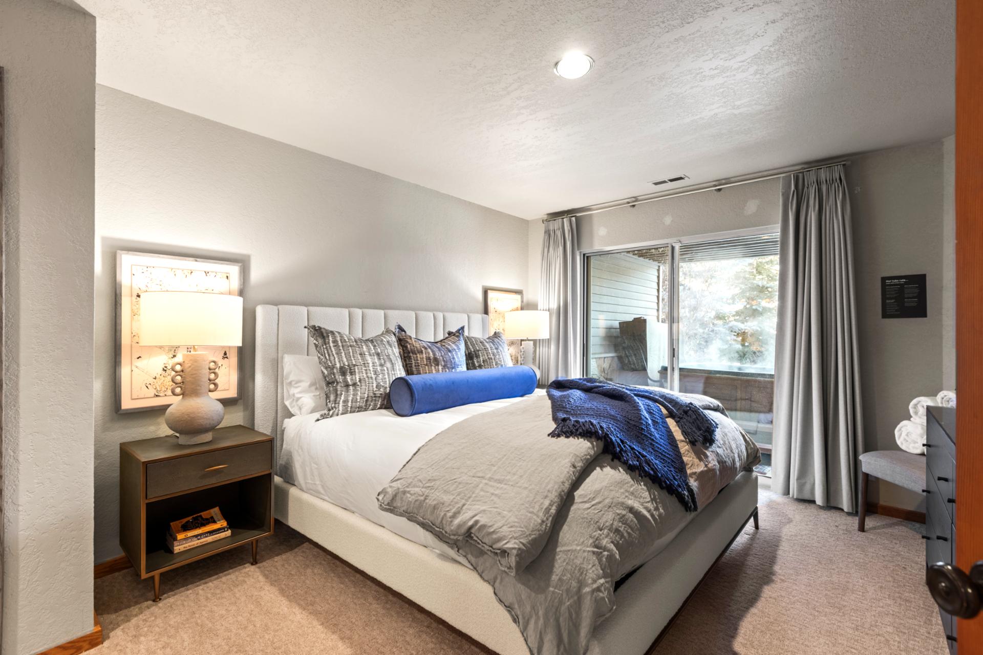 Relaxing guest bedroom with plush bedding, sliding glass door, and serene natural views.