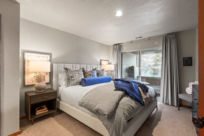 Relaxing guest bedroom with plush bedding, sliding glass door, and serene natural views.