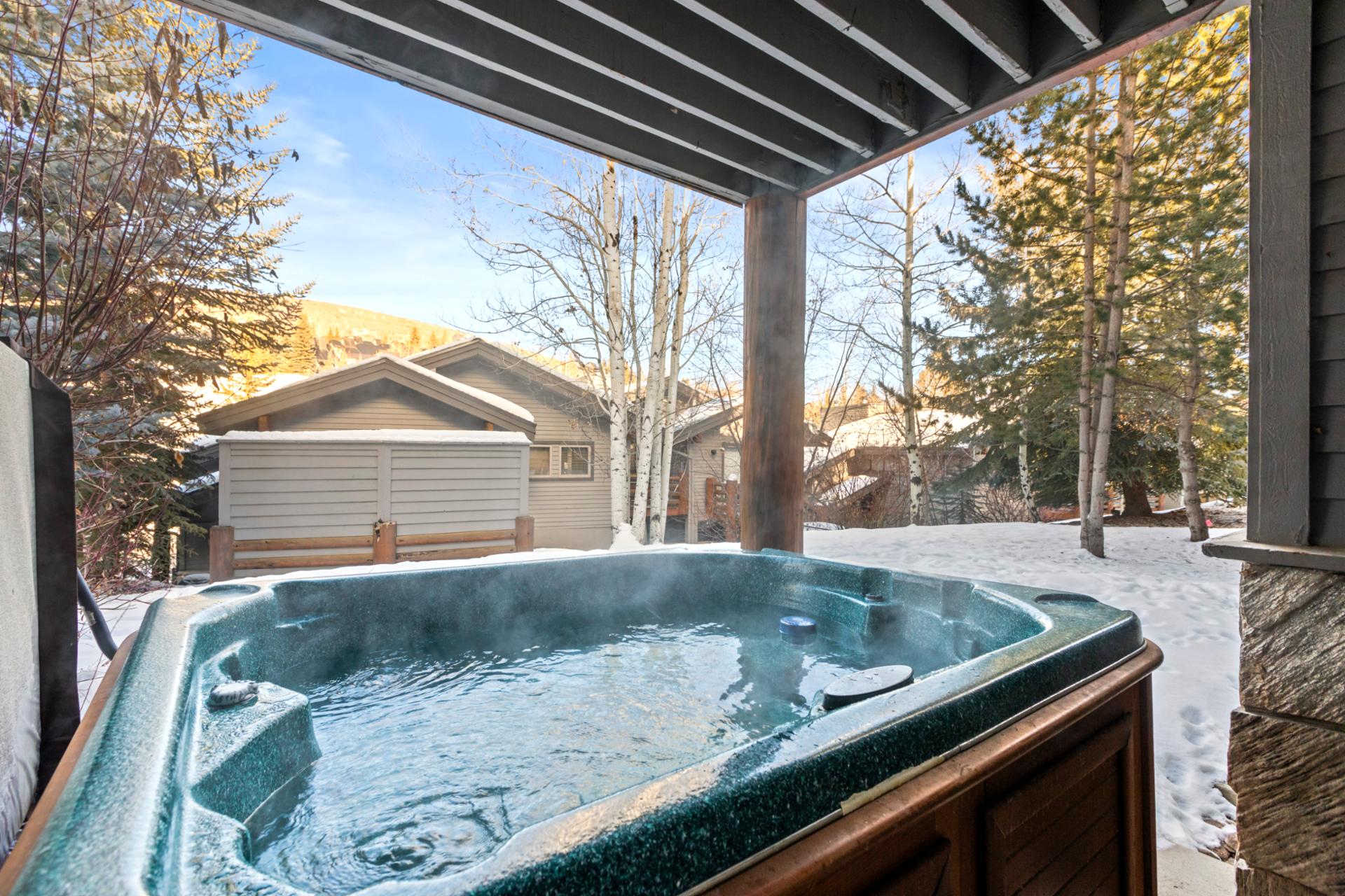 Cozy outdoor hot tub retreat with snowy mountain views and evergreen trees.