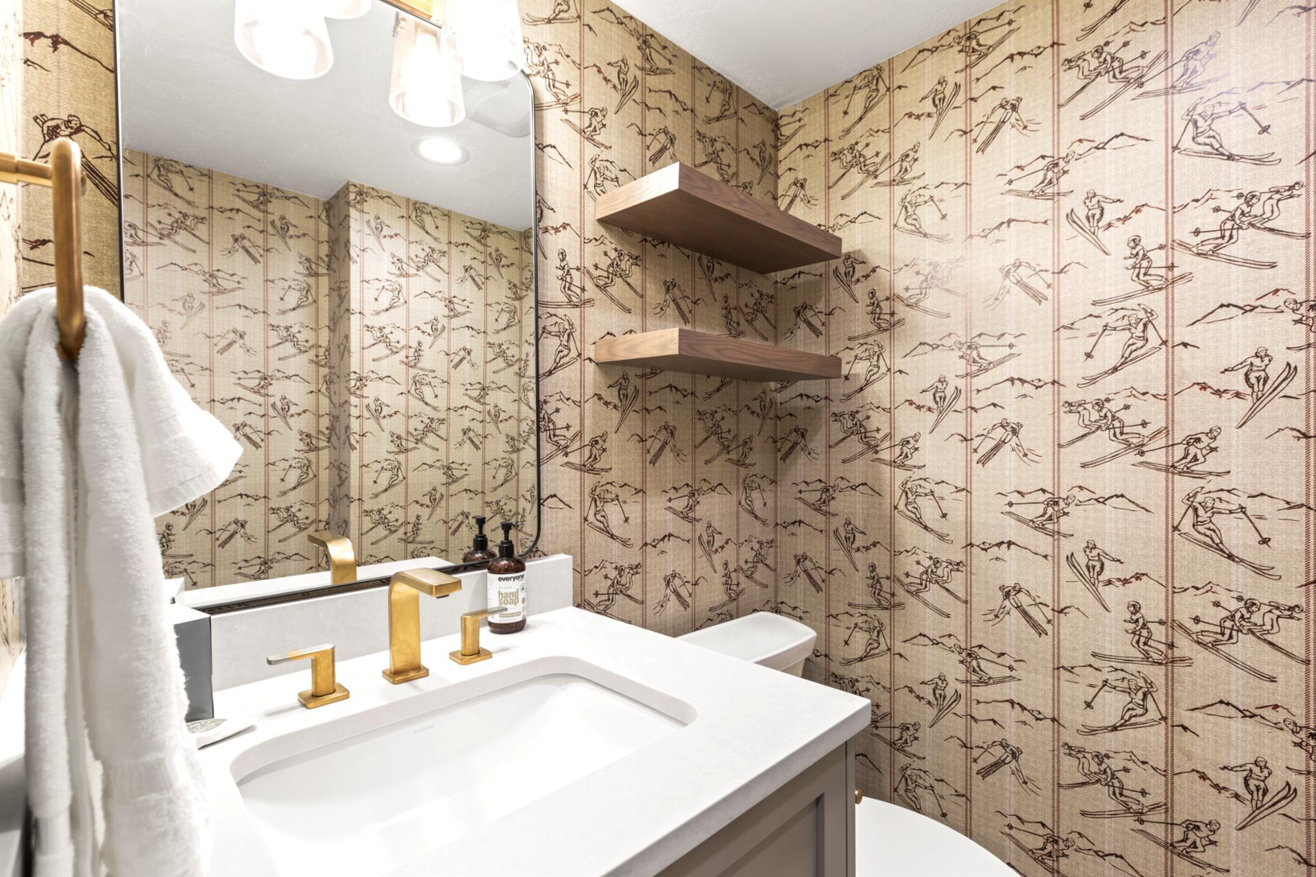 Stylish powder room with ski-themed wallpaper, gold fixtures, and a clean modern touch.