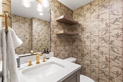 Stylish powder room with ski-themed wallpaper, gold fixtures, and a clean modern touch.
