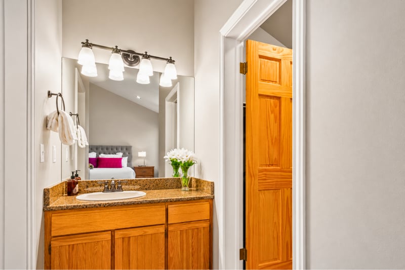 Powder bath with granite vanity opens toward the primary bedroom's tufted headboard