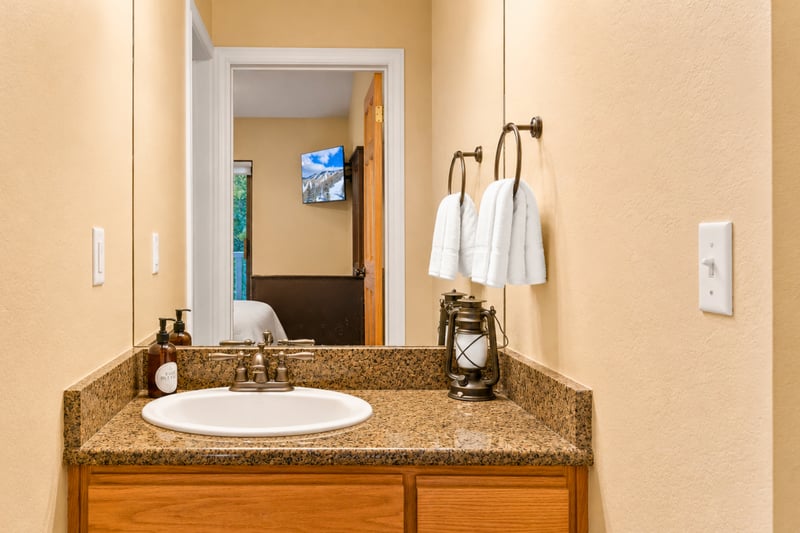 Bathroom vanity with granite counter and mirror reflecting the hallway TV nook