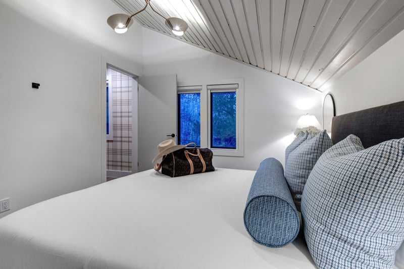 Upper-level bedroom with vaulted tongue-and-groove ceiling and forest-view windows