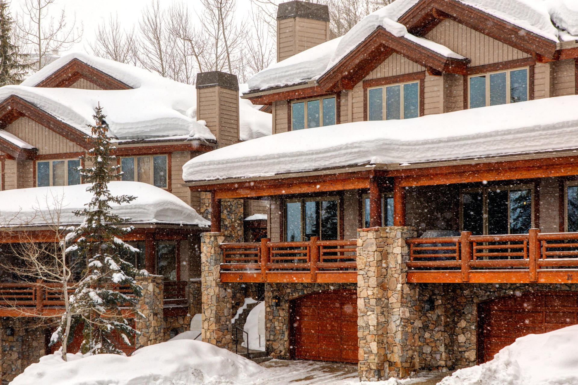 A classic mountain townhome wrapped in stone and timber, with a private garage and balconies framed by soft snowfall and alpine views.