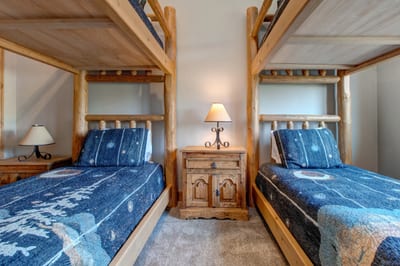 This cozy upper-level bunk room features two Twin-over-Twin log bunk beds with soft carpeting and warm lighting. Perfect for kids or extra guests.