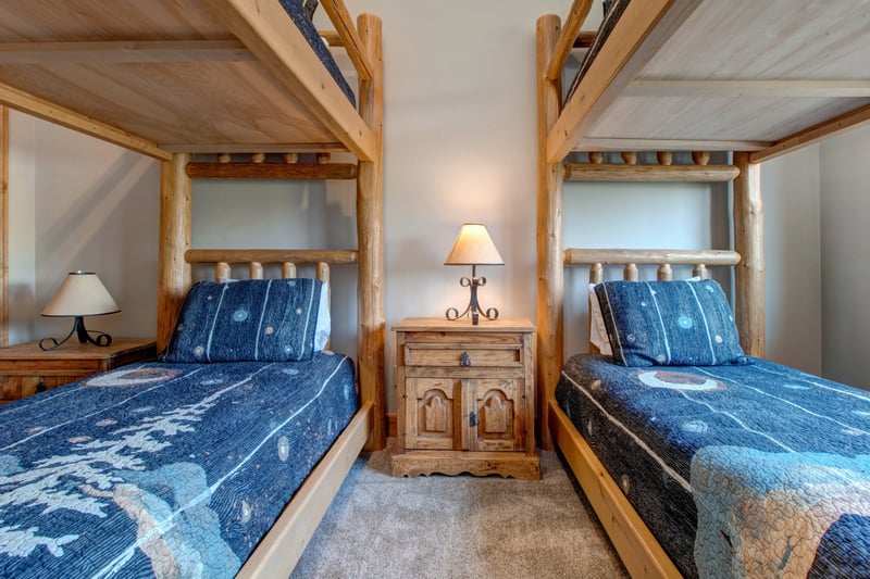 This cozy upper-level bunk room features two Twin-over-Twin log bunk beds with soft carpeting and warm lighting. Perfect for kids or extra guests.