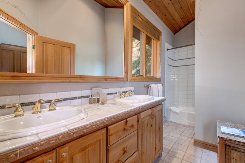 Bright bathroom with dual sinks, wood accents, and tiled shower.