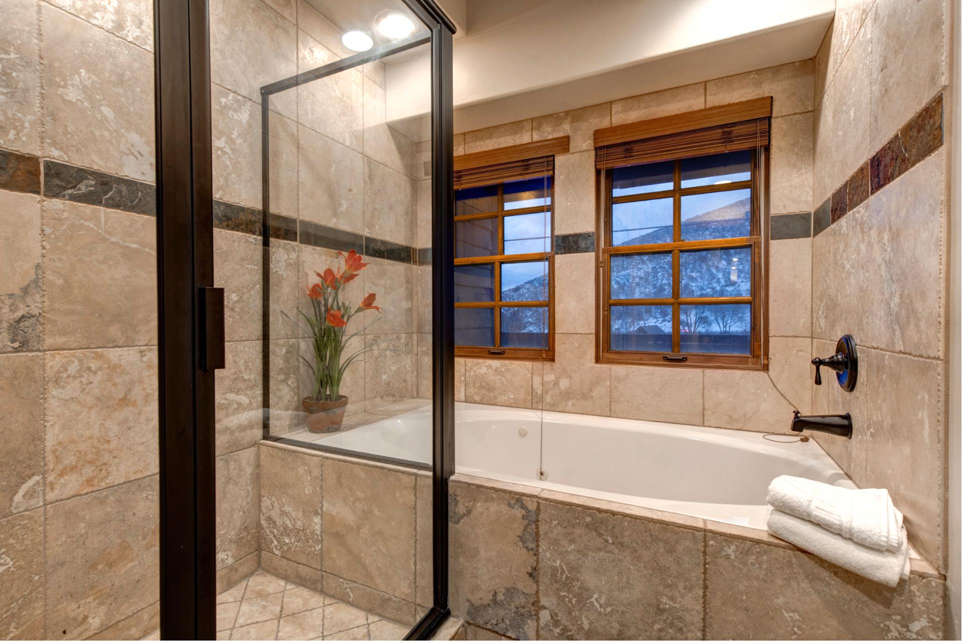 Tiled tub and shower combo with scenic window view and stylish dark accents.