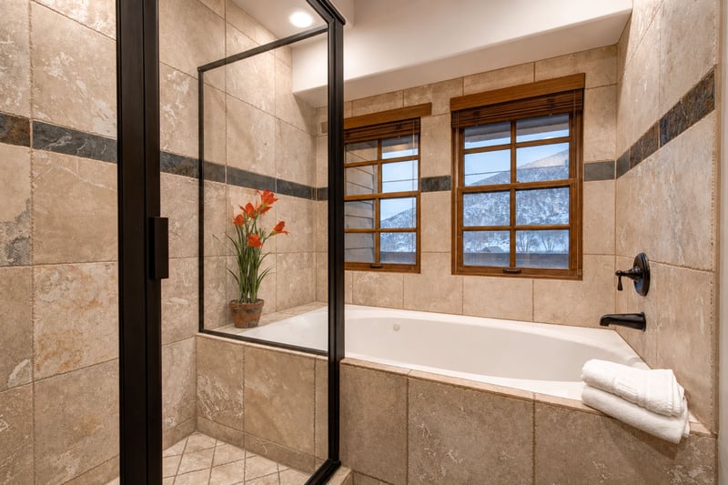 Tiled tub and shower combo with scenic window view and stylish dark accents.