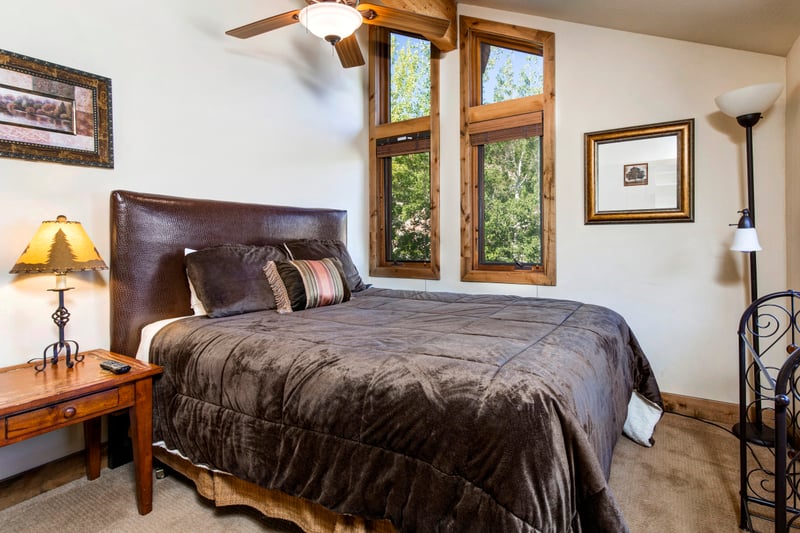 Cozy bedroom with leather headboard, wooden furniture, and nature views.